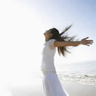 woman standing on beach in the sun with arms spread out and face up to the sun