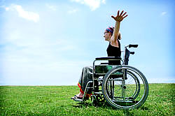 Photo of girl in wheelchair in grassy field with arms out like flying