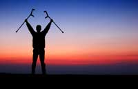 person with crutches standing with sunset behind them
