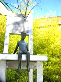 photo: sculpture of a boy sitting on chair with tree growing from his head